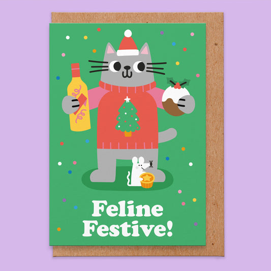 Christmas card that has a green background with an illustration of a grey cat wearing a Christmas jumper holding a bottle of eggnog and a pudding. Stop at the cat's foot there is a white mouse with a mince pie. The card reads feline festive!