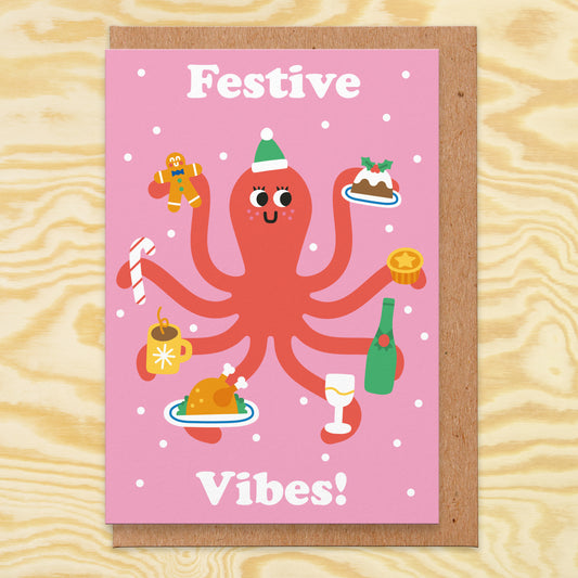 Christmas card that reads Festive Vibes  with an octopus on holding a gingerbread person, Christmas pudding, mince pie, champagne and glass, turkey, hot chocolate and candy cane.
