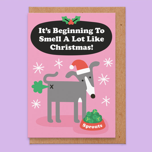 Christmas card that reads it's beginning to smell a lot like Christmas! With an illustration of a grey whippet (or it could be an Italian greyhound) with a dog bowl full of sprouts and a green fart.