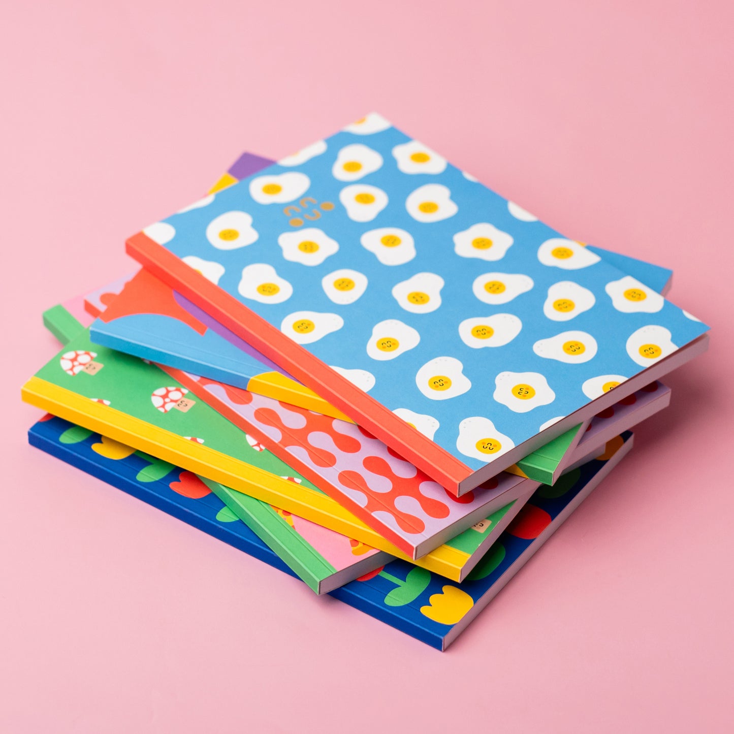 a stack of colourful notebooks with various cute patterns on them including eggs, mushrooms and flowers