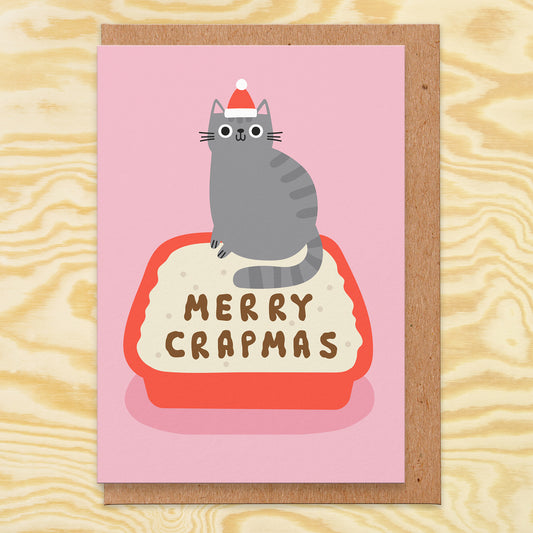 Christmas card with an illustration of a grey cat wearing a Santa hat stood at the top of a litter tray. The poop spells out merry crapmas.