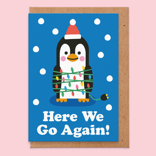 Christmas card that reads here we go again! With an illustration of a penguin with lots of fairy lights wrapped around it.