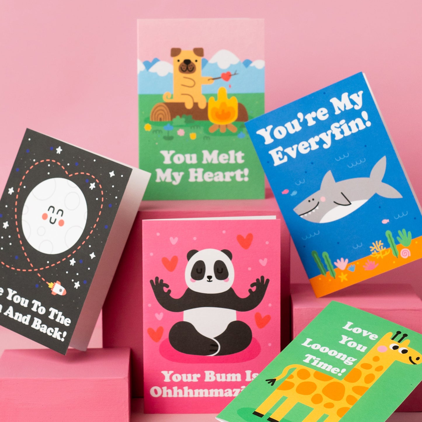 photograph of five valentine's day cards featuring a panda, a giraffe, a shark, a dog and the moon on a pink background arranged beautifully