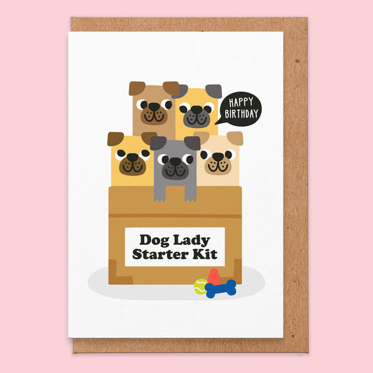 White greetings card with an illustration of five pugs in a cardboard box that has a label on it that says dog lady starter kit. One of the pugs has a speech bubble coming from it that says happy birthday.