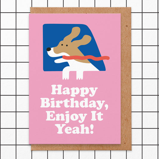 Pink birthday card with an illustration of a dogs head out of a window with its ears and tongue blowing in the wind. The wording is happy birthday, enjoy it yeah!