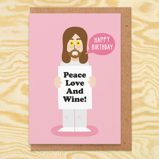 Pink greetings card with an illustration of John holding a sign that says peace love and wine. There is a speech bubble saying happy birthday.
