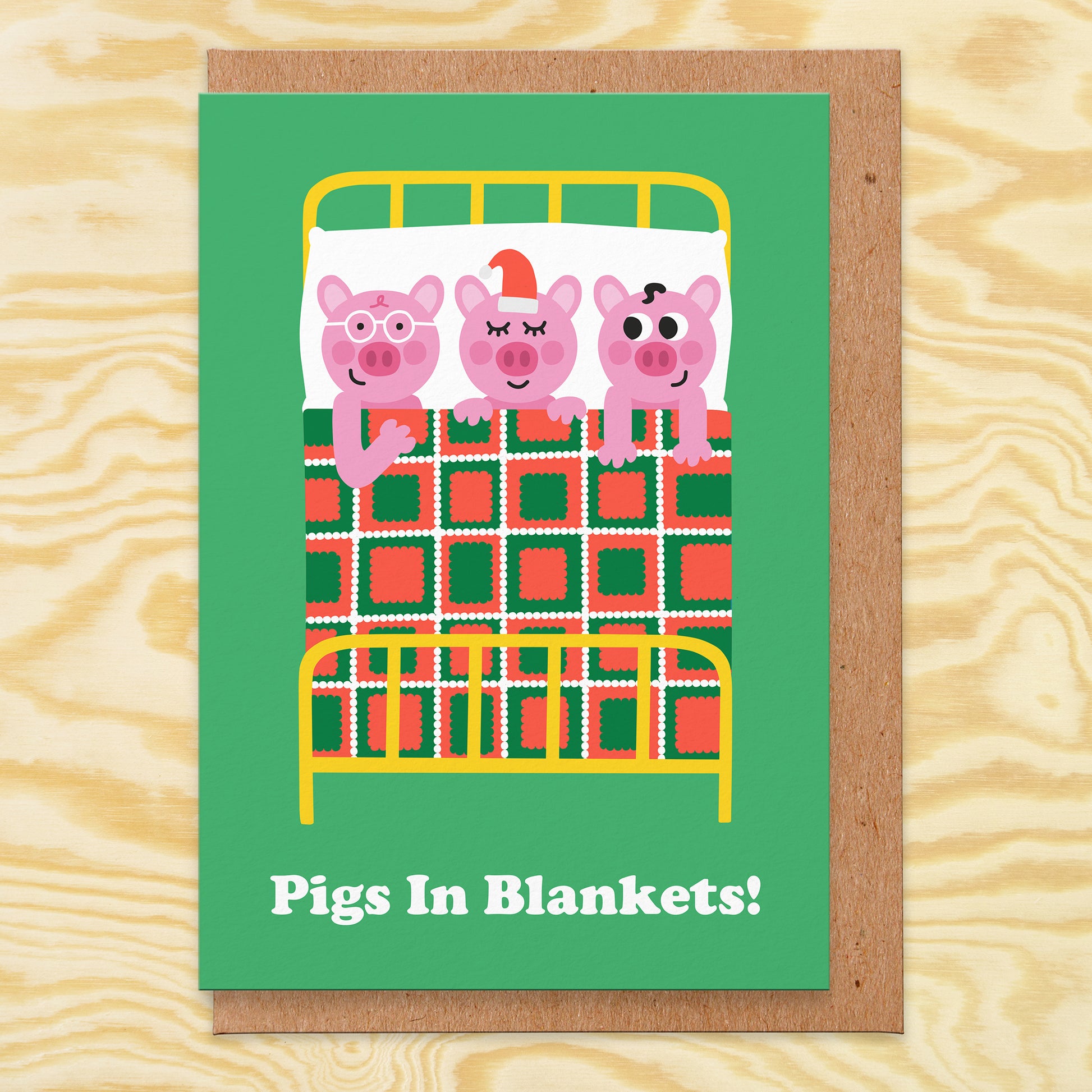 Christmas card with an illustration of 3 pigs in bed under a blanket and it reads pigs in blankets!